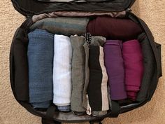 an open suitcase filled with folded clothes on the floor next to a carpeted wall