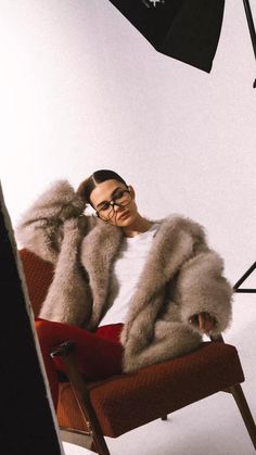 a woman sitting in a chair wearing a fur coat