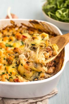 a casserole dish with spinach and cheese being lifted by a wooden spoon