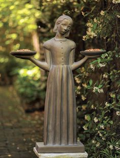 a statue holding a tray with food on it in front of some bushes and flowers