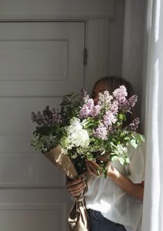 a woman holding a bouquet of flowers in front of her face while looking out the window