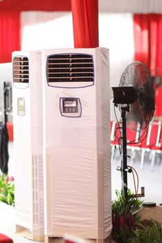 an air conditioner sitting on top of a table next to a red chair and fan