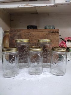 four mason jars sitting on top of a counter next to a wooden box and flowers