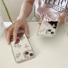 a woman sitting at a table with two cell phones in front of her and one holding the phone