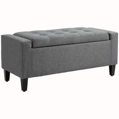 a gray bench with wooden legs and a button tufted cushion on the bottom, in front of a white background