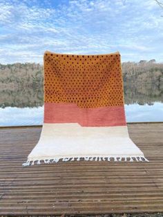 an orange and white blanket sitting on top of a wooden floor next to a body of water