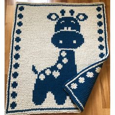 a crocheted blanket with a blue and white design on it, sitting on a wooden floor