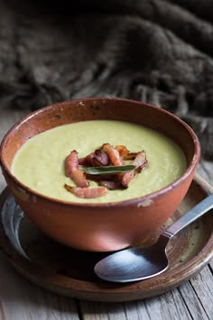 a brown bowl filled with soup on top of a wooden table next to a spoon