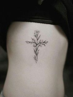 a cross tattoo on the side of a woman's stomach, with flowers growing out of it