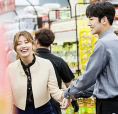 a man and woman holding hands while standing in front of a grocery store display case