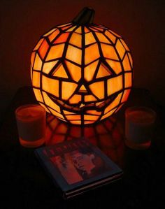 a lighted pumpkin sitting on top of a table next to two candles and a book