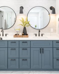 two round mirrors are above the double sinks in this white and gray bathroom with black faucets