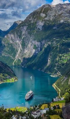 a cruise ship in the water surrounded by mountains and greenery on a sunny day