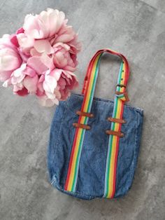 a denim bag with rainbow straps next to a pink peonie flower on the floor