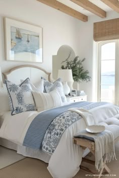 a white bed with blue and white comforter in a bedroom next to a window