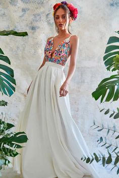 a woman wearing a white dress with colorful flowers in her hair standing next to plants