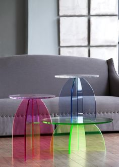 two colorful tables sitting on top of a wooden floor next to a gray couch in a living room