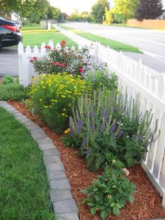 a white picket fence next to a flower bed