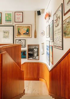 the stairs are lined with framed pictures and posters on the wall above them is a wooden handrail