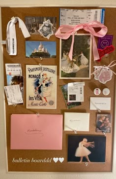 a cork board with pictures, cards and magnets on it's side that has a pink ribbon hanging from the top