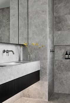 a bathroom with grey marble walls and flooring, two sinks and a shower stall