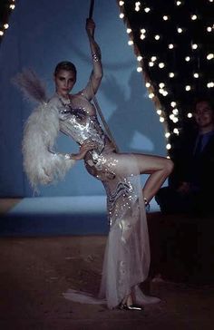 a woman in a silver and white dress is holding a pole with feathers on it