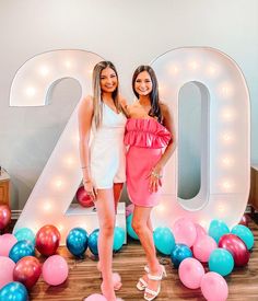 two women standing next to each other in front of balloons and letters that spell out the number twenty