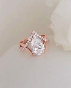 a close up of a diamond ring on a white surface with a flower in the background