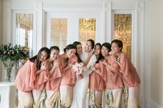 a group of women standing next to each other in front of a white wall holding bouquets