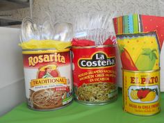 three cans of food sitting on top of a green table next to other containers and bags