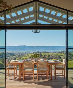 an outdoor dining area with wooden table and chairs, overlooking the mountains in the distance