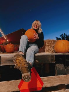 a woman sitting on top of a wooden bench holding a pumpkin