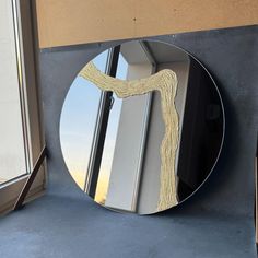 a round mirror sitting on the side of a wall next to a window sill