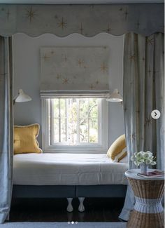 a white bed sitting under a window next to a table with a lamp on it