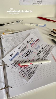 an open notebook sitting on top of a white table next to pens and pencils