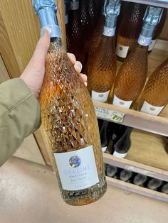 a person holding up a bottle of wine in front of shelves with bottles on it