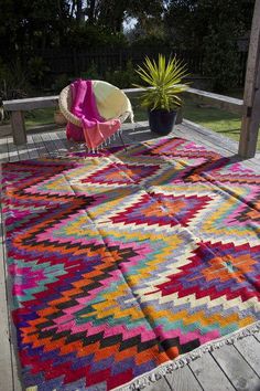 a multicolored rug sitting on top of a wooden deck next to a potted plant