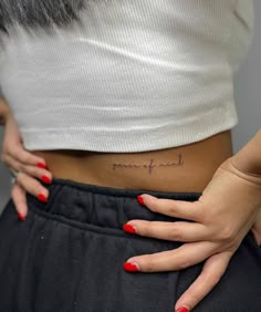 a woman's stomach with the word peace tattooed on her lower belly and red nail polish