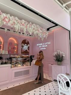 a woman standing in front of a pink bakery with white flowers hanging from the ceiling