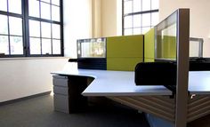 an office cubicle with desks and chairs in front of two large windowed windows