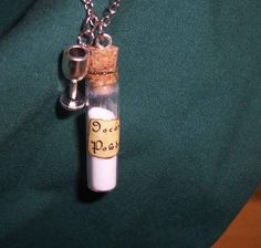 a small bottle with a cork is sitting on a green cloth and has a chain attached to it