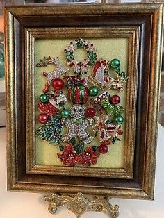 a framed christmas ornament on display in a gold frame with red, green and white ornaments