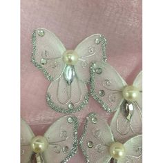 three white butterflies with pearls on them and some beads in the middle, sitting on a pink fabric