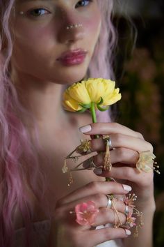 a woman with pink hair holding a flower in her hand and wearing rings around her fingers