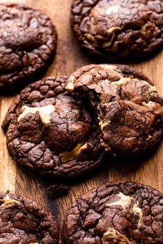 chocolate cookies with white butter on top and one broken in half sitting on a wooden surface