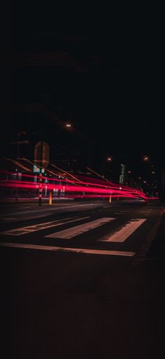 an empty city street at night with traffic lights streaking across the road and buildings in the background