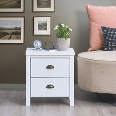 a small white table with two drawers and a clock on the side next to it