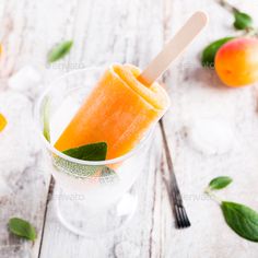 an orange ice cream popsicle in a clear cup with mint and peaches around it