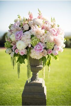 a tall vase filled with pink and white flowers on top of a green field next to grass