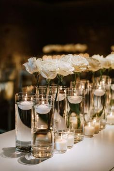 white roses and candles are arranged in vases on a long table with glass holders